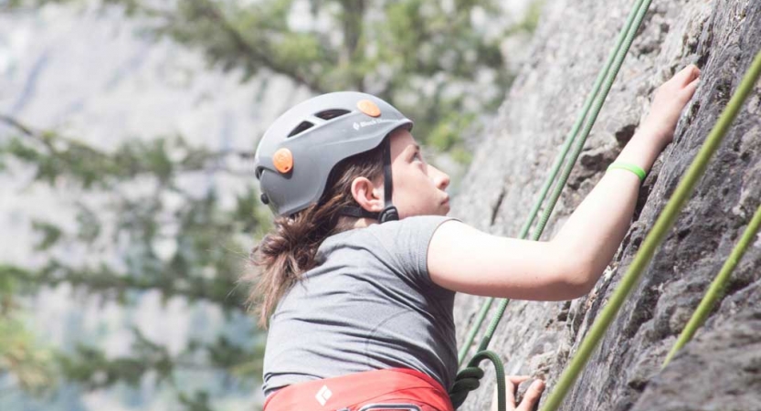 an outward bound student wearing safety gear focuses as they climb a rock facing